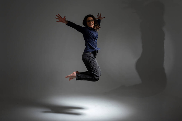 Портрет веселой позитивной девушки, прыгающей в воздух с поднятыми кулаками, смотрящей в камеру, изолированной на светлом фоне, сдержанной клавишей. Энергетическая концепция жизни людей. Место для надписи - Фото, изображение