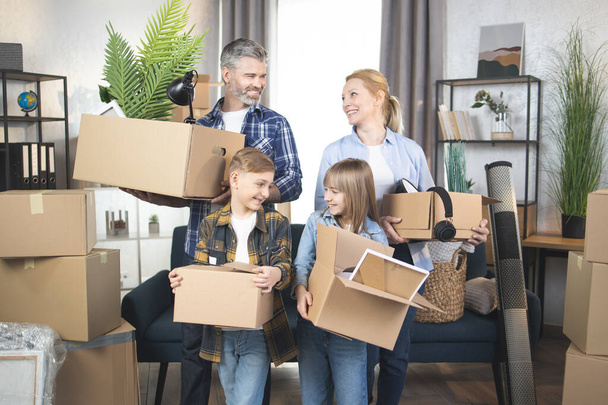 Happy Caucasian family with kids standing with boxes at new apartment - Foto, afbeelding