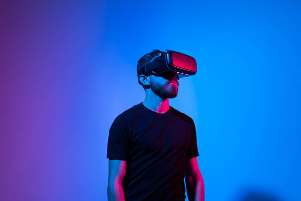 Young bearded man in virtual reality helmet plays online game in metaverse. Game simulates behavior in fictional world, gadgets and virtual reality addiction. Future technology concept. - Photo, Image