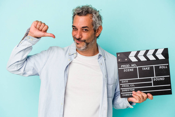 Middle age caucasian man holding a clapperboard isolated on blue background  feels proud and self confident, example to follow. - Фото, изображение