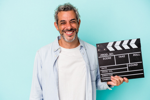 Middle age caucasian man holding a clapperboard isolated on blue background  happy, smiling and cheerful. - Foto, Imagen