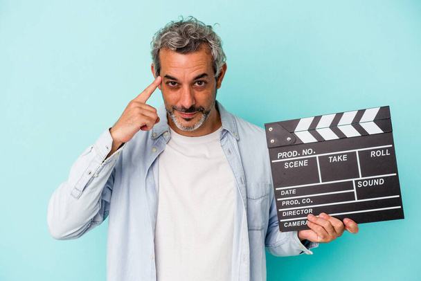 Middle age caucasian man holding a clapperboard isolated on blue background  pointing temple with finger, thinking, focused on a task. - Foto, Imagen