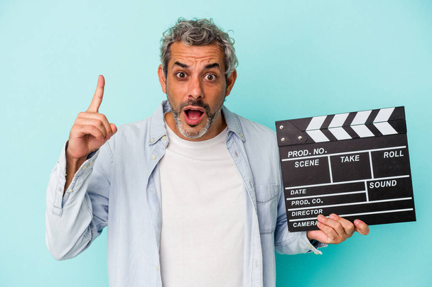 Middle age caucasian man holding a clapperboard isolated on blue background  having an idea, inspiration concept. - Foto, Imagen