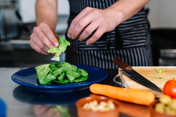 λεπτομέρεια από τα χέρια ενός νεαρού επικεφαλής, προετοιμασία ένα πιάτο σαλάτα σε μια επαγγελματική κουζίνα. - Φωτογραφία, εικόνα