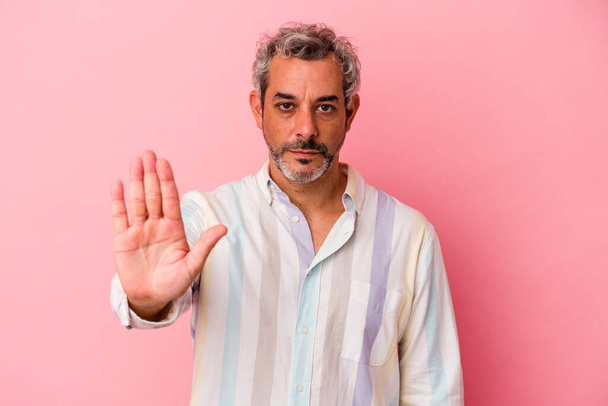 Middelbare leeftijd blanke man geïsoleerd op roze achtergrond staan met uitgestrekte hand tonen stopteken, voorkomen dat u. - Foto, afbeelding