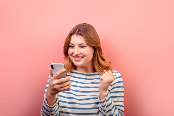 Retrato de linda menina de cabelos castanhos alegres espantados usando dispositivo de telefone 5g post aplicativo como reação isolada sobre fundo cor pastel rosa. Conceito de felicidade. - Foto, Imagem