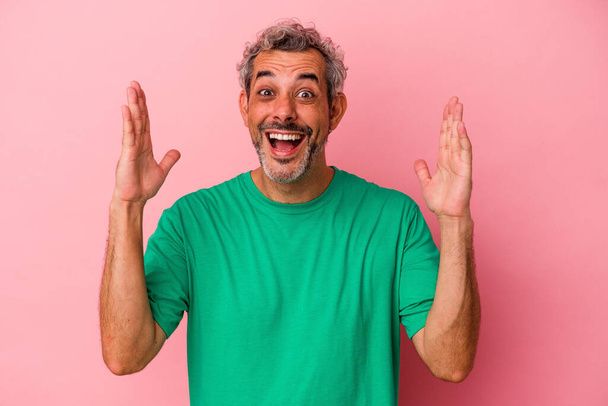Middle age caucasian man isolated on pink background  receiving a pleasant surprise, excited and raising hands. - Foto, Imagen