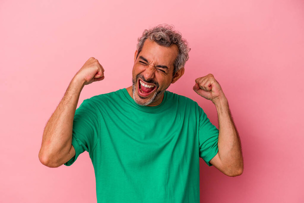 Middle age caucasian man isolated on pink background  raising fist after a victory, winner concept. - Zdjęcie, obraz