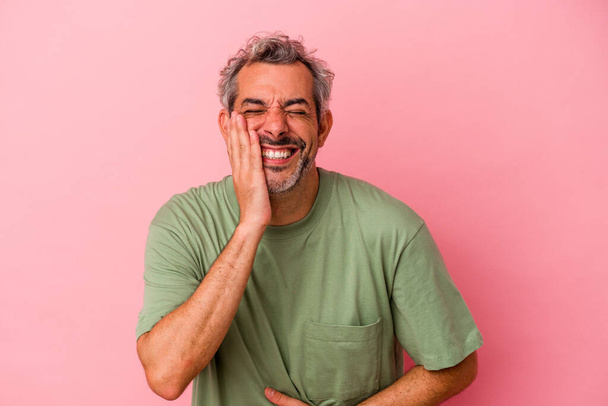 Homem caucasiano de meia idade isolado em fundo rosa ri alegremente e se diverte mantendo as mãos no estômago. - Foto, Imagem