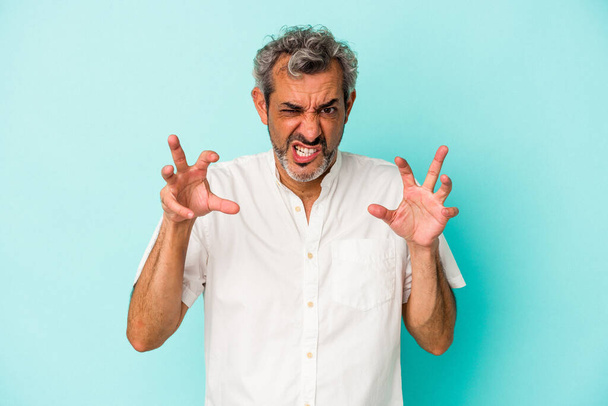 Middle age caucasian man isolated on blue background  showing claws imitating a cat, aggressive gesture. - Photo, Image