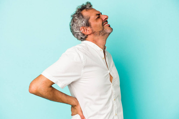 Middle age caucasian man isolated on blue background  suffering a back pain. - 写真・画像