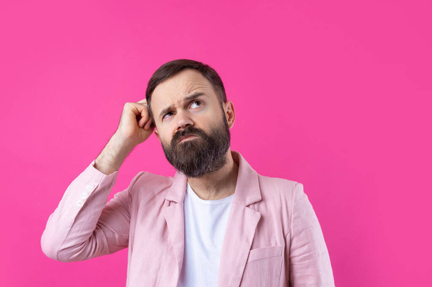 Handsome man with a beard in a pink jacket is thinking over an isolated red background. - Foto, imagen