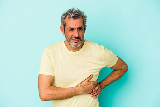 Homem caucasiano de meia idade isolado em fundo azul com dor de fígado, dor de estômago. - Foto, Imagem