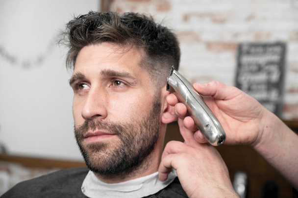Man barber cutting hair of male client with clipper at barber shop. Hairstyling process.  - Photo, Image