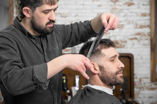 Парикмахер стрижет ножницами волосы красивому молодому человеку . - Фото, изображение