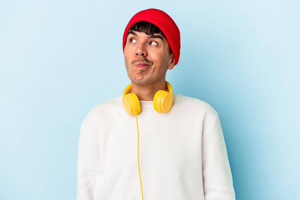 Nuori sekarotuinen mies, joka kuuntelee sinisellä taustalla eristettyä musiikkia unelmoiden tavoitteiden ja päämäärien saavuttamisesta - Valokuva, kuva