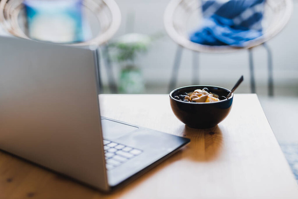 eating mango blueberries oatmeal while working from home on a laptop, concept of remote working or lunch at the office - Fotoğraf, Görsel
