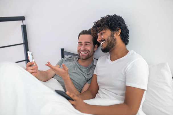 Cheerful man pointing at his cellphone screen to his boyfriend - Φωτογραφία, εικόνα