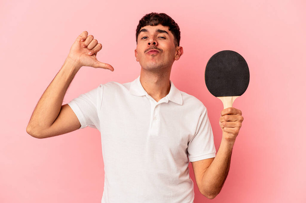 Jeune homme métis tenant une raquette de ping-pong isolé sur fond rose se sent fier et confiant, exemple à suivre. - Photo, image