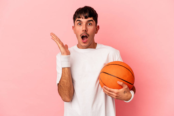 Jonge gemengde ras man basketbal geïsoleerd op roze achtergrond verrast en geschokt. - Foto, afbeelding