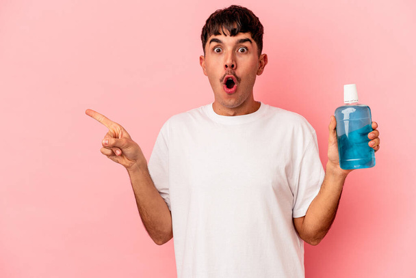 Young mixed race man holding mouthwash isolated on pink background pointing to the side - Foto, afbeelding