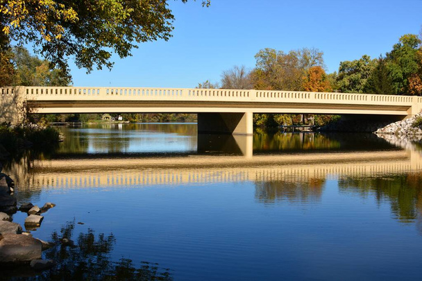 Acque calme che scorrono sul Fox River. Un nuovo bellissimo ponte sul fiume Fox in autunno con acqua che scorre sotto la struttura lungo il fiume Fox. Alberi di colori autunnali con acque azzurre riflettenti e cielo azzurro in un pomeriggio d'autunno mozzafiato.  - Foto, immagini