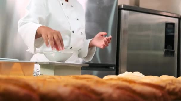 Zblízka kuchařova ruka v bílé kuchařské uniformě a zástěře měří a krájí syrové těsto, připravuje chléb, koláče a čerstvé pečivo, pečení v troubě v nerezové kuchyni restaurace. - Záběry, video