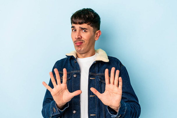 Jonge gemengde ras man geïsoleerd op blauwe achtergrond verwerpen iemand die een gebaar van walging. - Foto, afbeelding