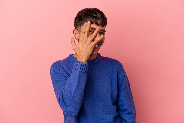 Young mixed race man isolated on pink background blink at the camera through fingers, embarrassed covering face. - Fotografie, Obrázek
