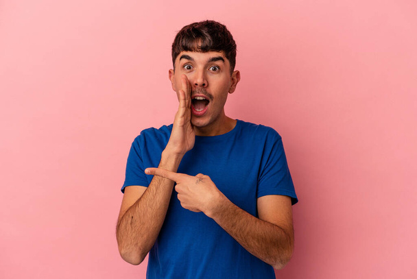 Young mixed race man isolated on pink background saying a gossip, pointing to side reporting something. - Foto, afbeelding