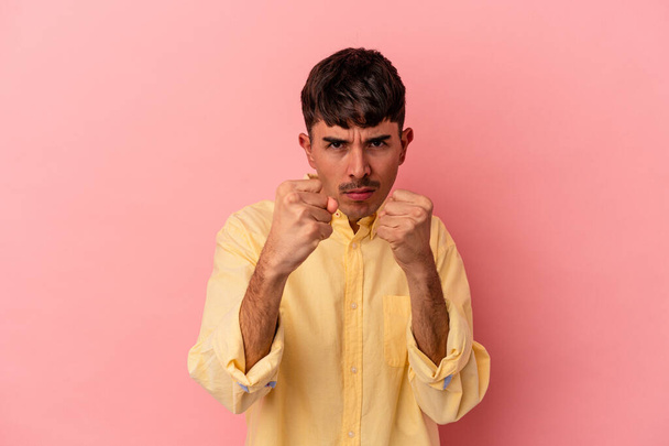 Молодой человек смешанной расы на розовом фоне показывает кулак к камере, агрессивное выражение лица. - Фото, изображение