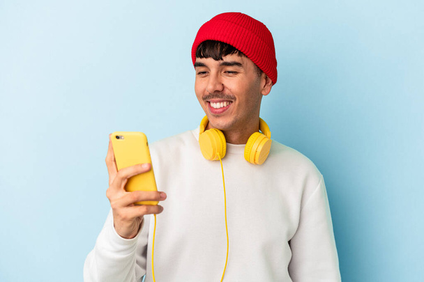 Young mixed race man listening to music isolated on blue background - Photo, image