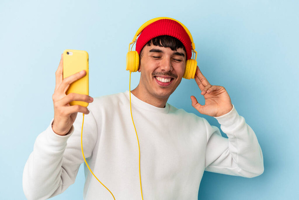 Молодий чоловік змішаної раси слухає музику ізольовано на синьому фоні
 - Фото, зображення