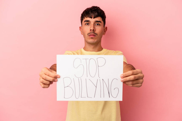 Young mixed race man holding stop bullying placard isolated on pink background - Foto, Bild