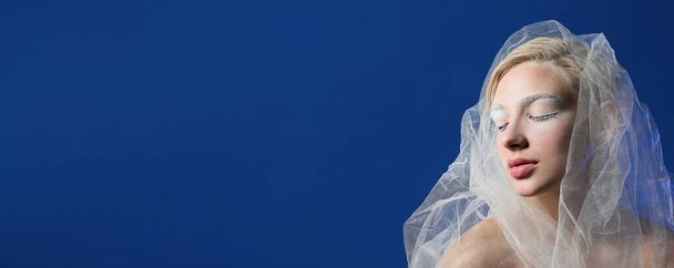 Όμορφη νεαρή γυναίκα με δημιουργικό μακιγιάζ και πέπλο σε μπλε φόντο με χώρο για κείμενο - Φωτογραφία, εικόνα