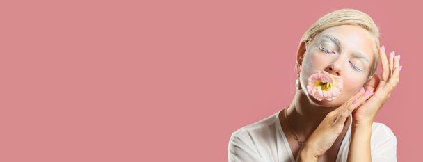 Όμορφη νεαρή γυναίκα με δημιουργικό μακιγιάζ και λουλούδι σε ροζ φόντο με χώρο για κείμενο - Φωτογραφία, εικόνα