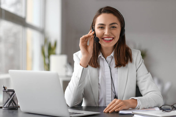 Pretty businesswoman with headset sitting at table in office - Foto, imagen