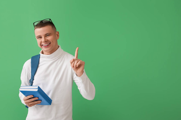 Male student with books pointing at something on green background - Фото, зображення