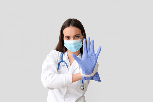 軽い背景で停止ジェスチャーを示す医療用マスクの若い女性医師。免疫概念 - 写真・画像