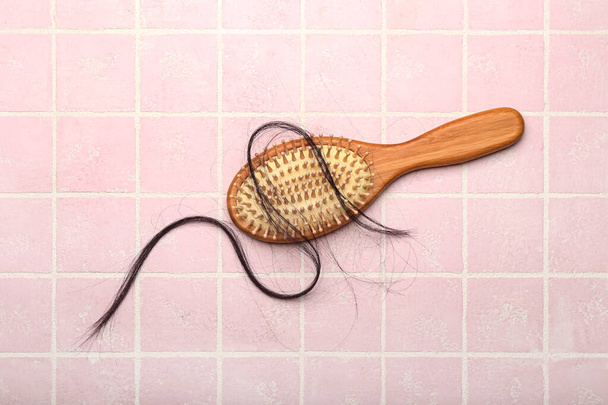 Кисть с выпавшими волосами на розовом фоне плитки - Фото, изображение