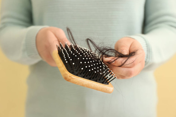 Woman holding brush with fallen down brunette hair on yellow background, closeup - 写真・画像
