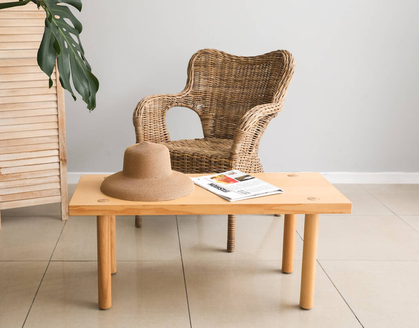 Mesa de madera con sombrero, periódico y silla de mimbre en la habitación - Foto, Imagen