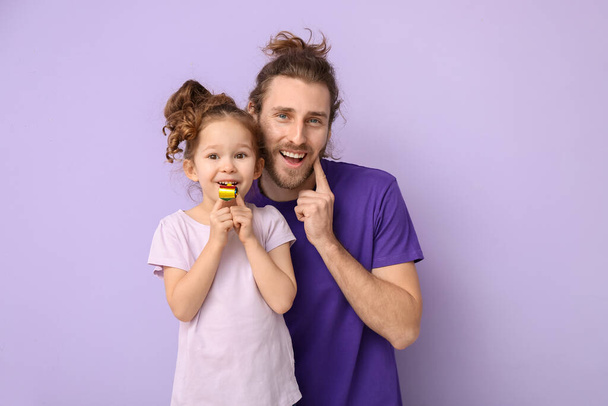 Lustiger Mann und ihre kleine Tochter mit Partygebläse auf fliederfarbenem Hintergrund. Aprilscherz-Fest - Foto, Bild