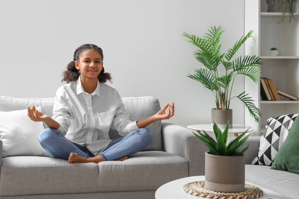 Afroamerikanische Teenager meditieren, während sie zu Hause auf dem Sofa sitzen - Foto, Bild