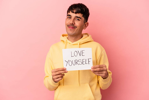 Молодой человек смешанной расы держит любовь себя плакат изолирован на розовом фоне - Фото, изображение