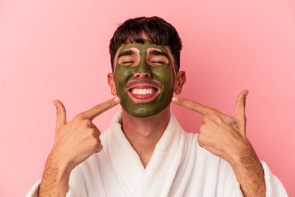 Junge gemischte Rasse Mann trägt Schönheit Gesichtsmaske isoliert auf rosa Hintergrund - Foto, Bild