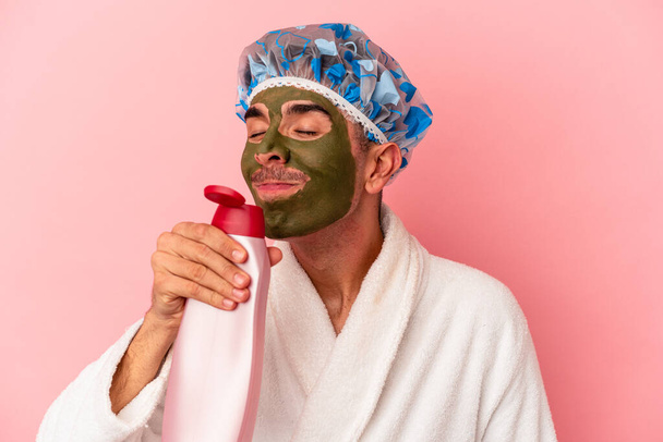Young mixed race man wearing beauty facial mask holding gel isolated on pink background - Valokuva, kuva