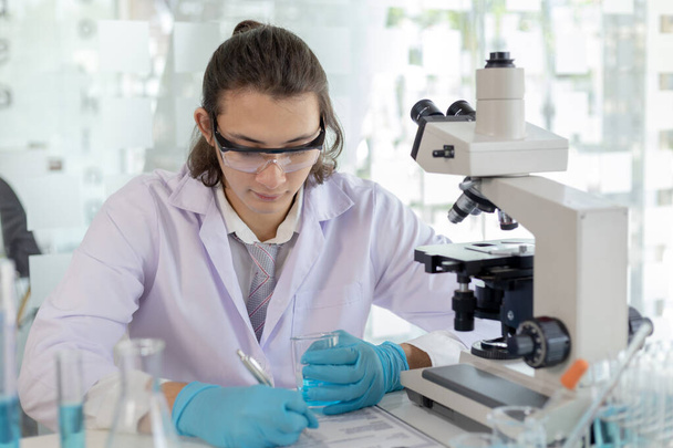 Laboratóriumi diagnózis szintetikus anyagok, tudós vagy kutató vizsgálja az anyag in vitro és rekord információk, Laboratóriumi kísérletek, Kutatók tudós működő elemzés kémcsővel. - Fotó, kép