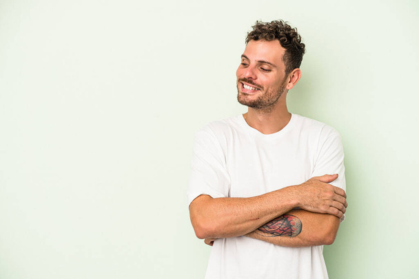 Young caucasian man isolated on green background smiling confident with crossed arms. - Photo, Image