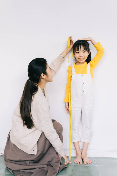 Asian mother is measuring her daughter's height - Valokuva, kuva